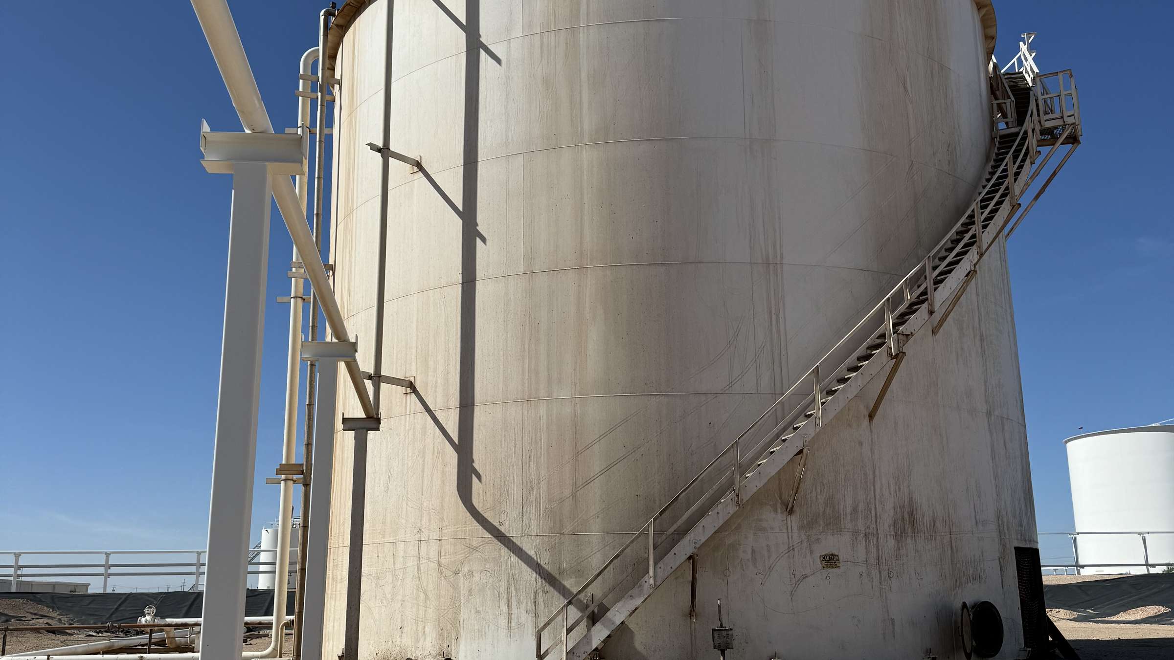 A large above-ground storage tank with an exterior stairway on a demolition site