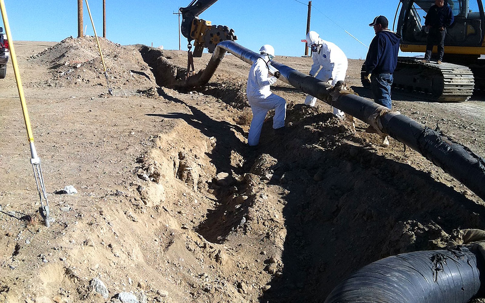 Crew in protective suits and respirators removing coated pipe from an open trench