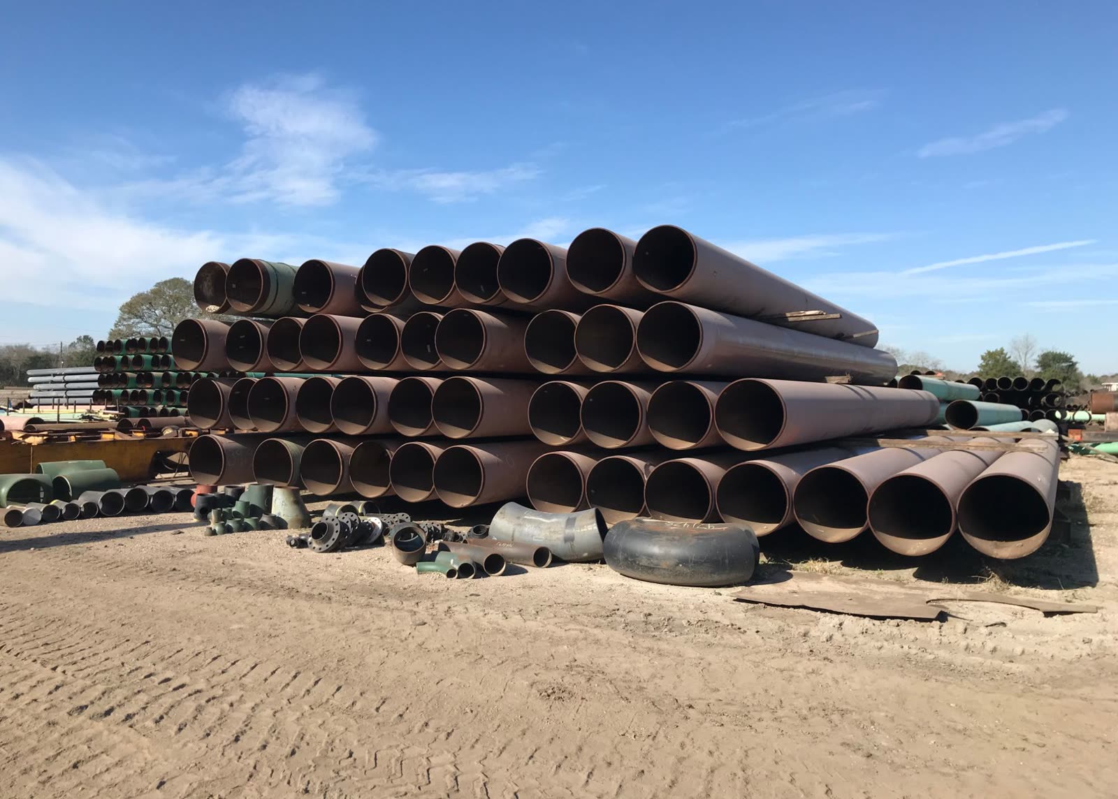 Retired large-diameter line pipe stacked in the yard with recovered fittings alongside